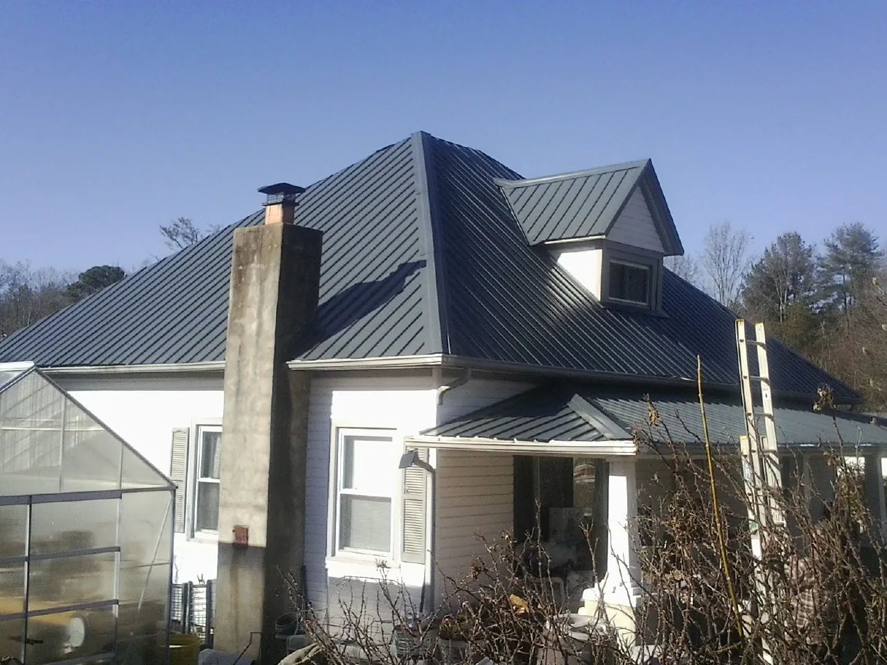 Dark blue standing seam metal roof on a white farmhouse with dormer — Slate & Tile Roof Repair by Roofing Brothers in Searsboro