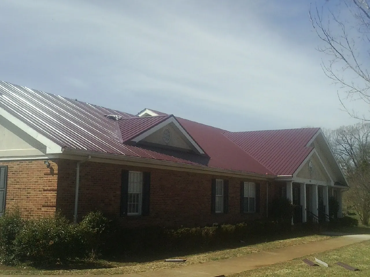 Red metal roof with gabled entries on a long brick building, from a Hail Damage Roof Repair job in Searsboro