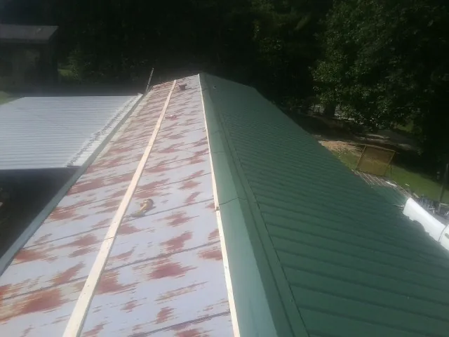 Old rusted panels beside newly installed green metal roofing — Wind Damage Roof Repair by Roofing Brothers in Searsboro