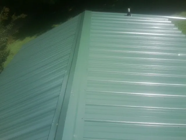 New green metal panels meeting at the ridge of a roof — Flat Roof Repair work by our crew in Searsboro