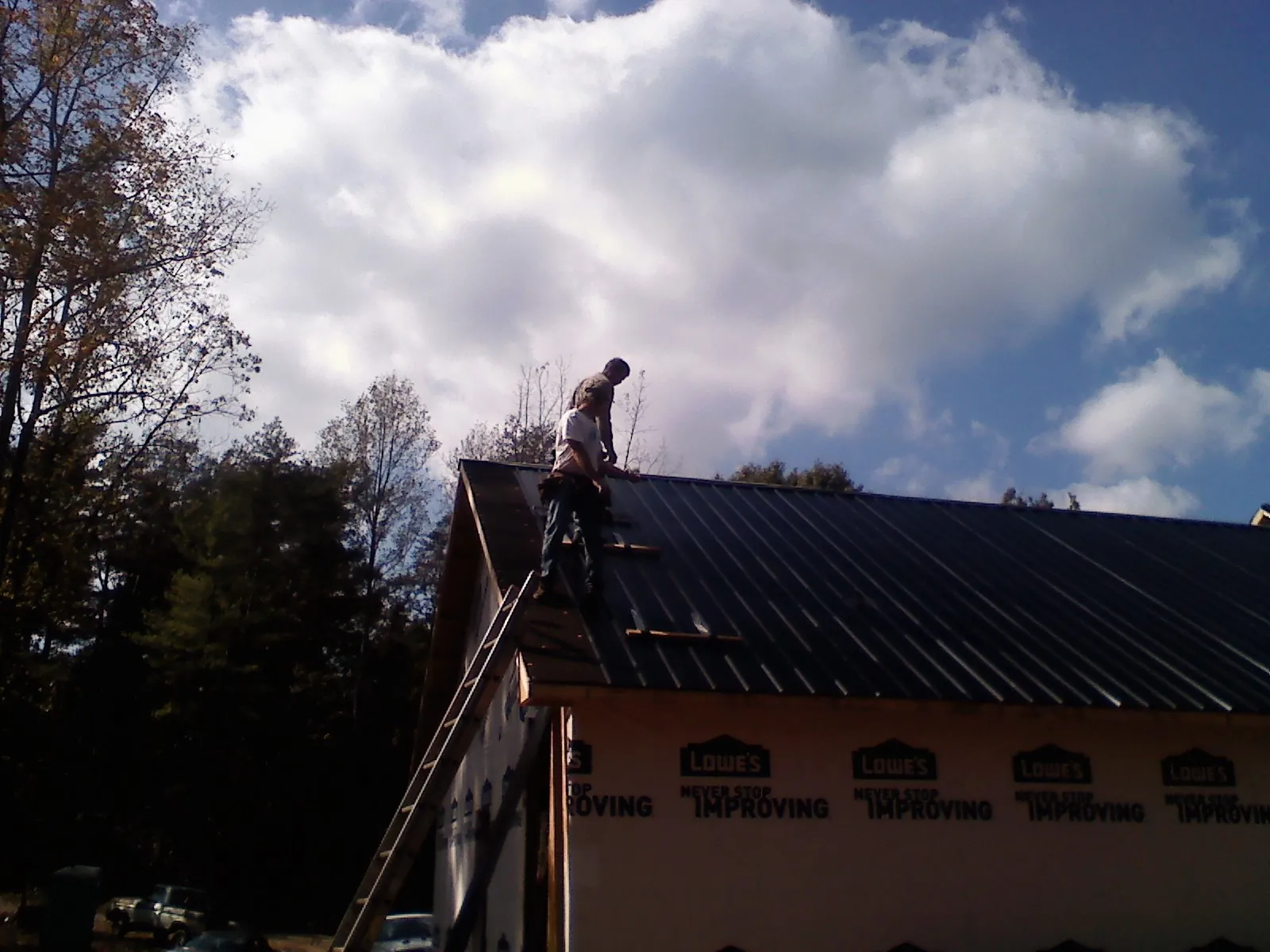 Roofer fastening dark metal panels high against a cloudy sky, from a Roof Inspection job in Searsboro