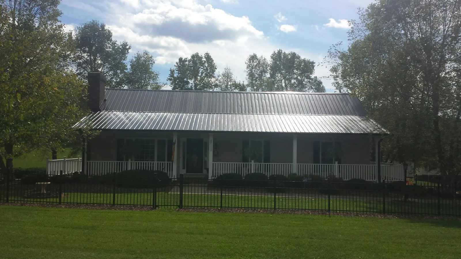 Gray metal roof on a brick ranch with a full width front porch — Gutter Guard Installation work by our crew in Searsboro