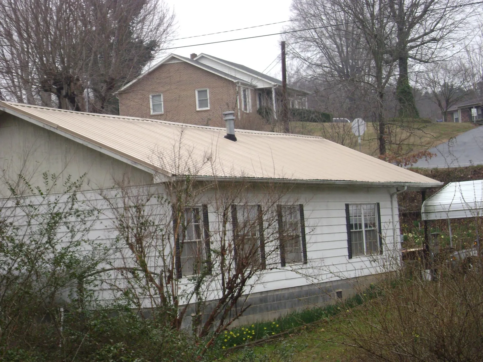 Tan metal roof on a white sided house set into a hillside — Commercial Roofing by Roofing Brothers in Searsboro