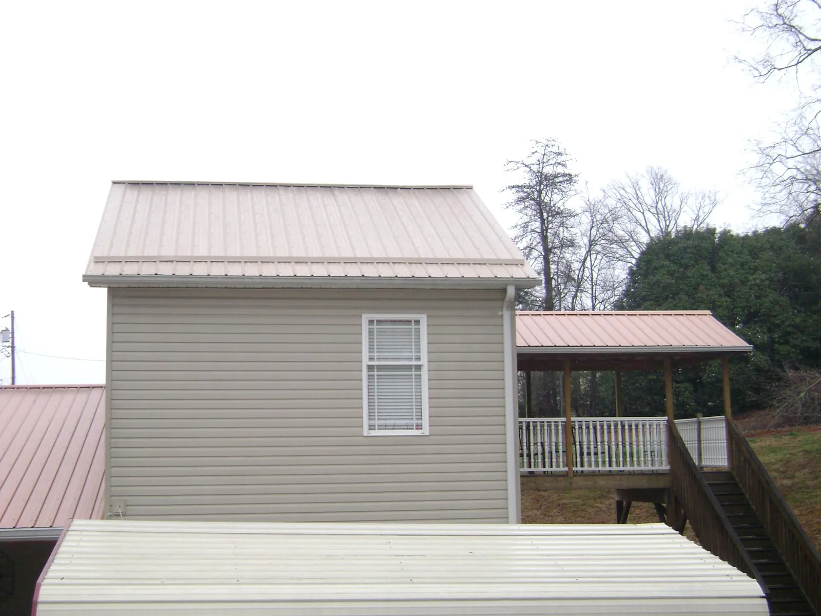 Tan metal roofs on a two story addition and attached porch, from a Roof Replacement job in Searsboro
